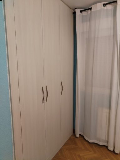 Armario blanco con puertas y cortina blanca a un lado. Pared azul detrás.