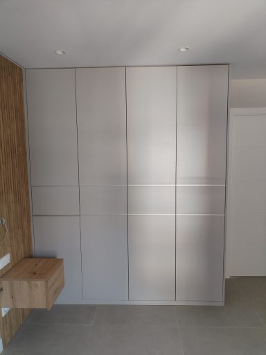 Armario moderno de puertas rectas en una pared con un acabado claro y mueble de madera al lado.