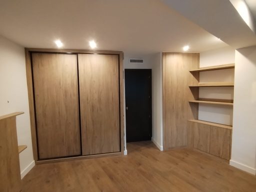 Habitación con paredes claras, armario de madera y estanterías, suelo de madera.
