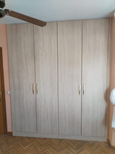 Armario de madera clara con puertas lisas y tiradores dorados en una habitación.
