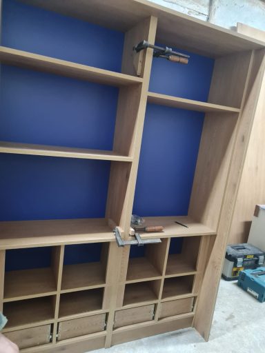Mueble de madera con compartimentos y fondo azul, en proceso de ensamblaje.