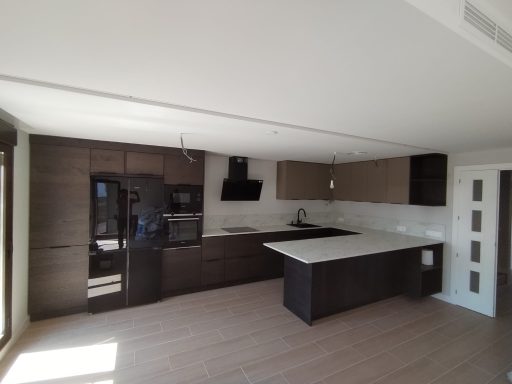 Cocina moderna con muebles oscuros, encimera blanca y electrodomésticos integrados.