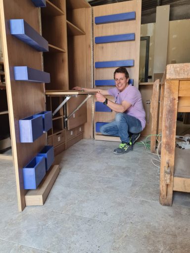 Hombre sonriente ajustando un estante de madera con cajas azules en un taller.