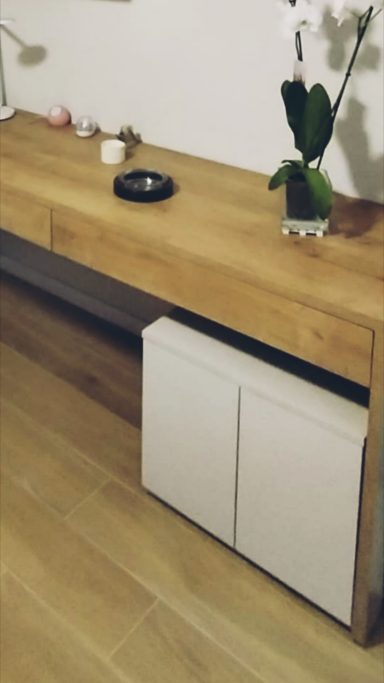 Mesa de madera con un espacio inferior para almacenamiento y una planta decorativa.