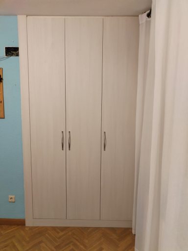Armario blanco de cuatro puertas en una pared azul, con una cortina al lado.