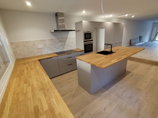 Cocina moderna con isla de madera, electrodomésticos empotrados y tonos neutros.