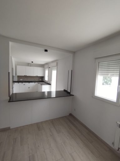 Cocina moderna con barra y ventanales iluminando el espacio. Suelo de madera clara.