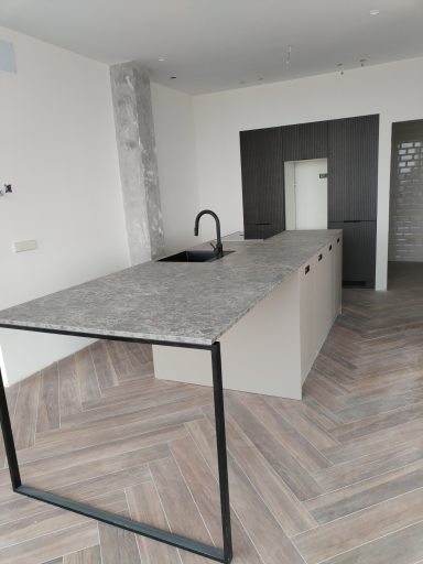 Cocina moderna con isla de concreto y fregadero, suelos de madera en patrón de espiga.