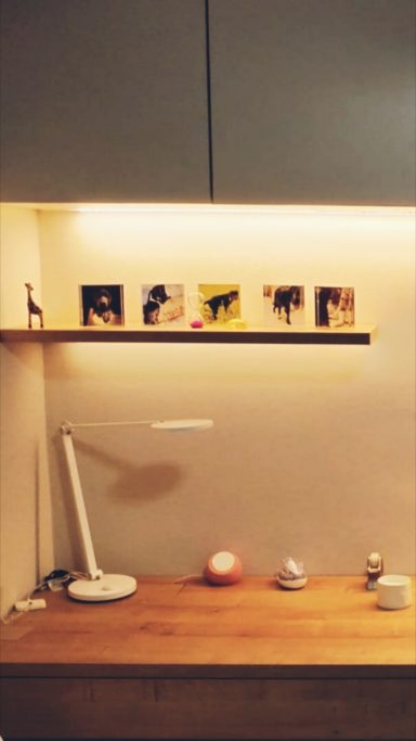 Estantería con fotos, una lámpara y decoración sobre una mesa de madera. Iluminación suave.