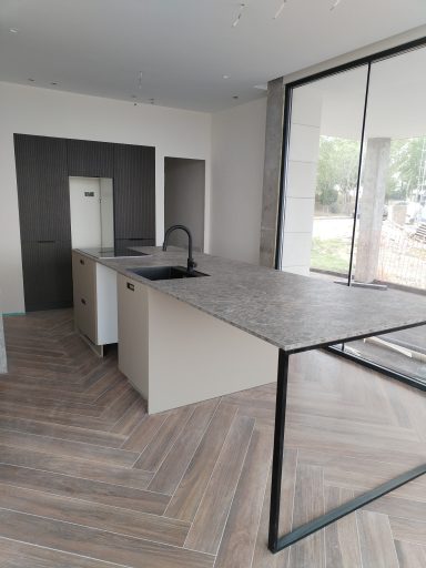Cocina moderna con isla, superficie de piedra y grandes ventanales. Suelo en espiga.