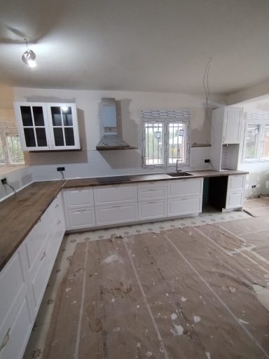 Cocina en proceso de remodelación con muebles blancos y suelo cubierto.