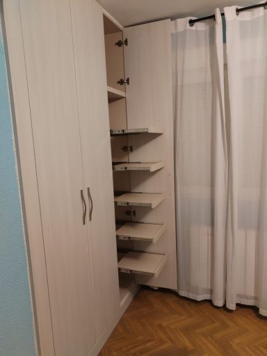Mueble de almacenamiento con estantes en un rincón, junto a una ventana cubierta con cortinas.