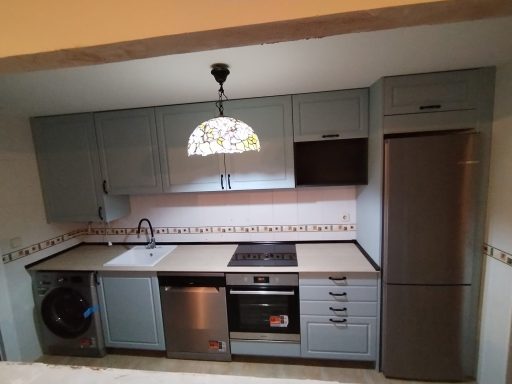 Cocina moderna con muebles grises, electrodomésticos de acero y una lámpara de techo.