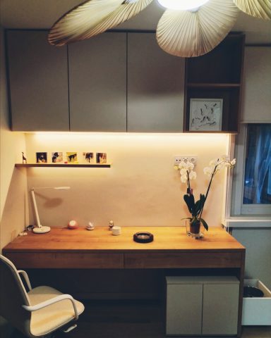 Escritorio moderno de madera con lámpara, floreros y estantería iluminada.