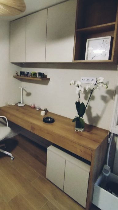 Escritorio de madera con silla, lámpara, planta y estantería. Pared clara y ambiente ordenado.